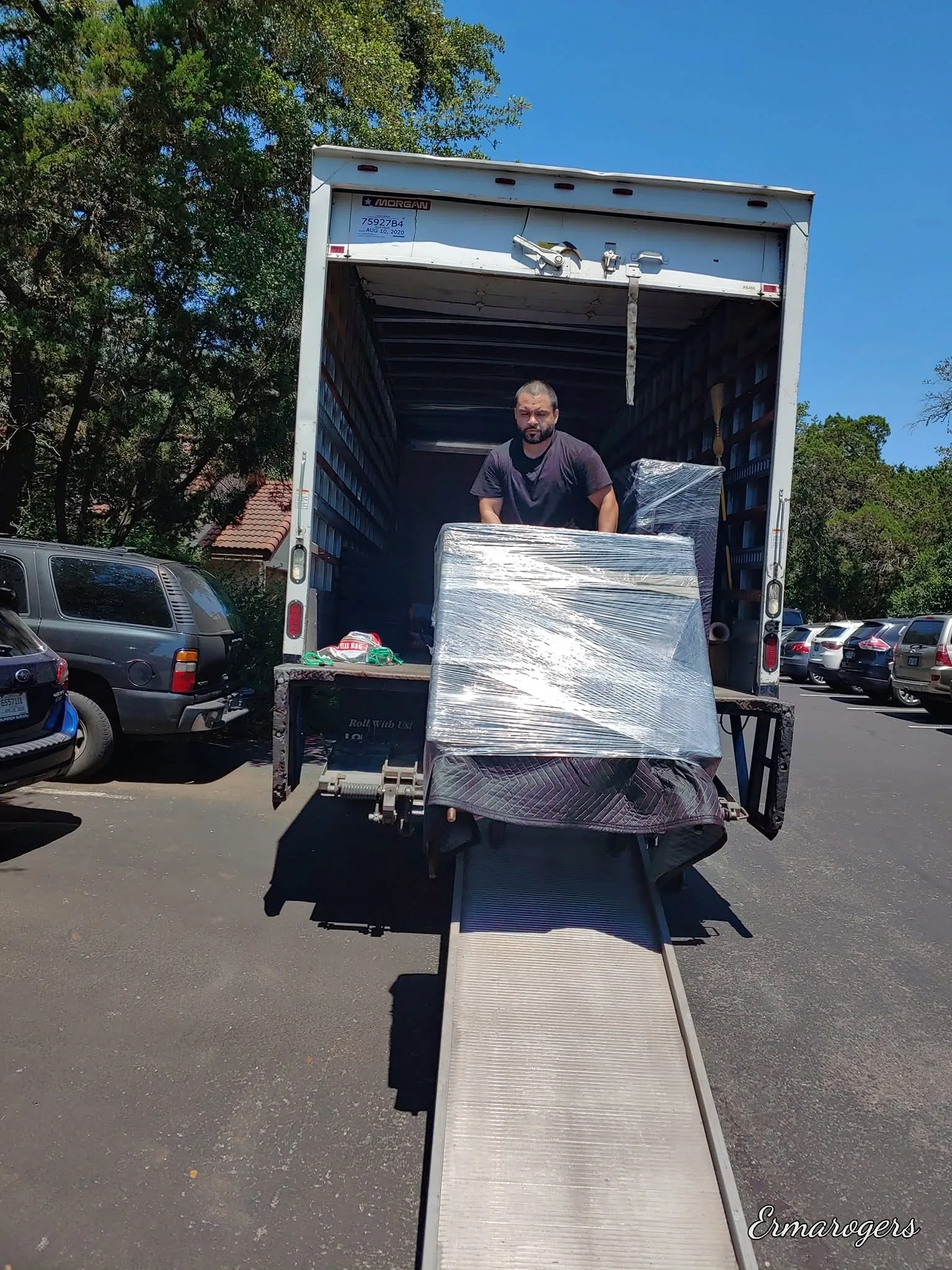Moving company worker loading wrapped furniture into a white Morgan moving truck with ramp extended.