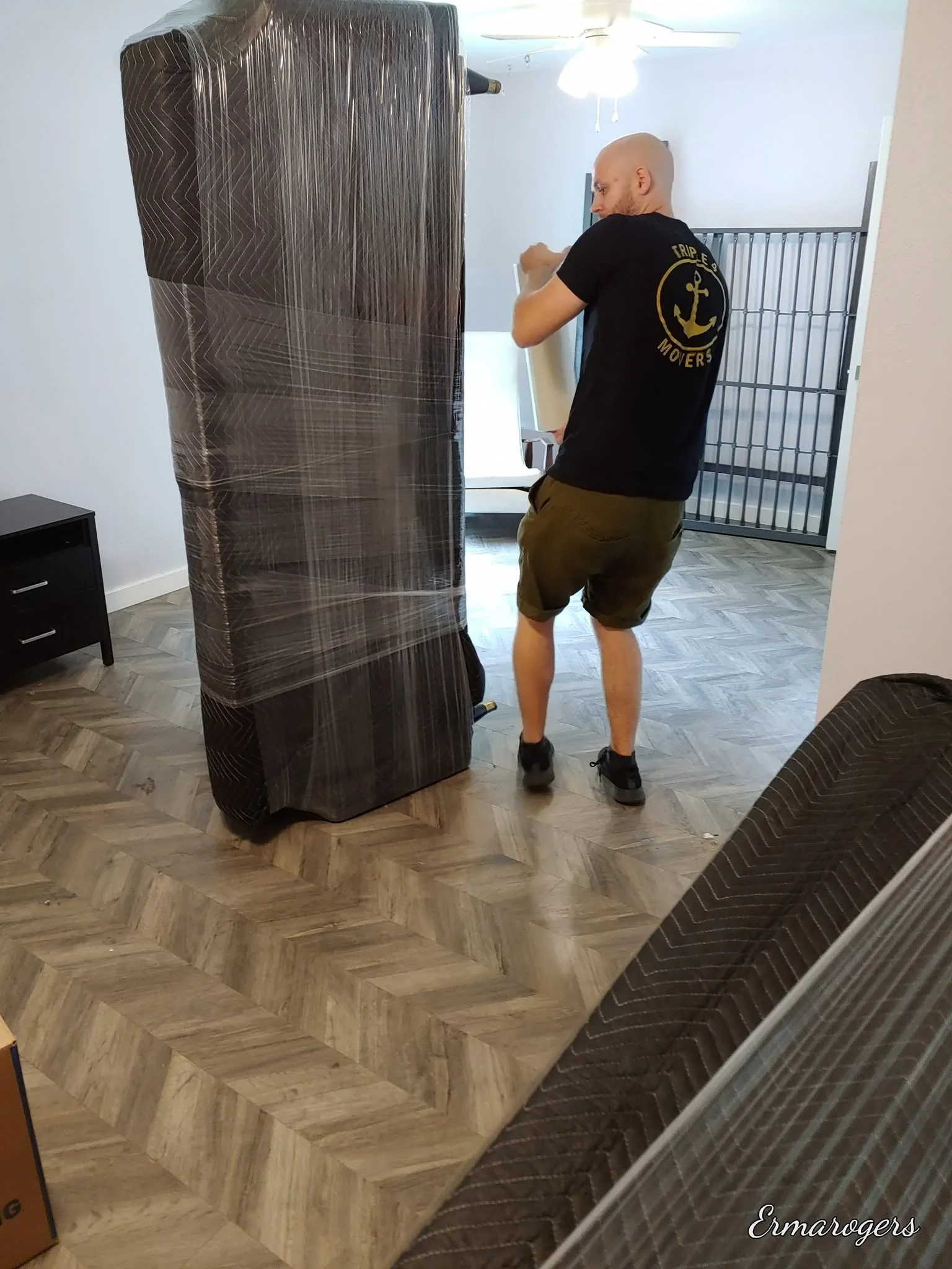Moving company worker wrapping a mattress in plastic on a wooden floor.