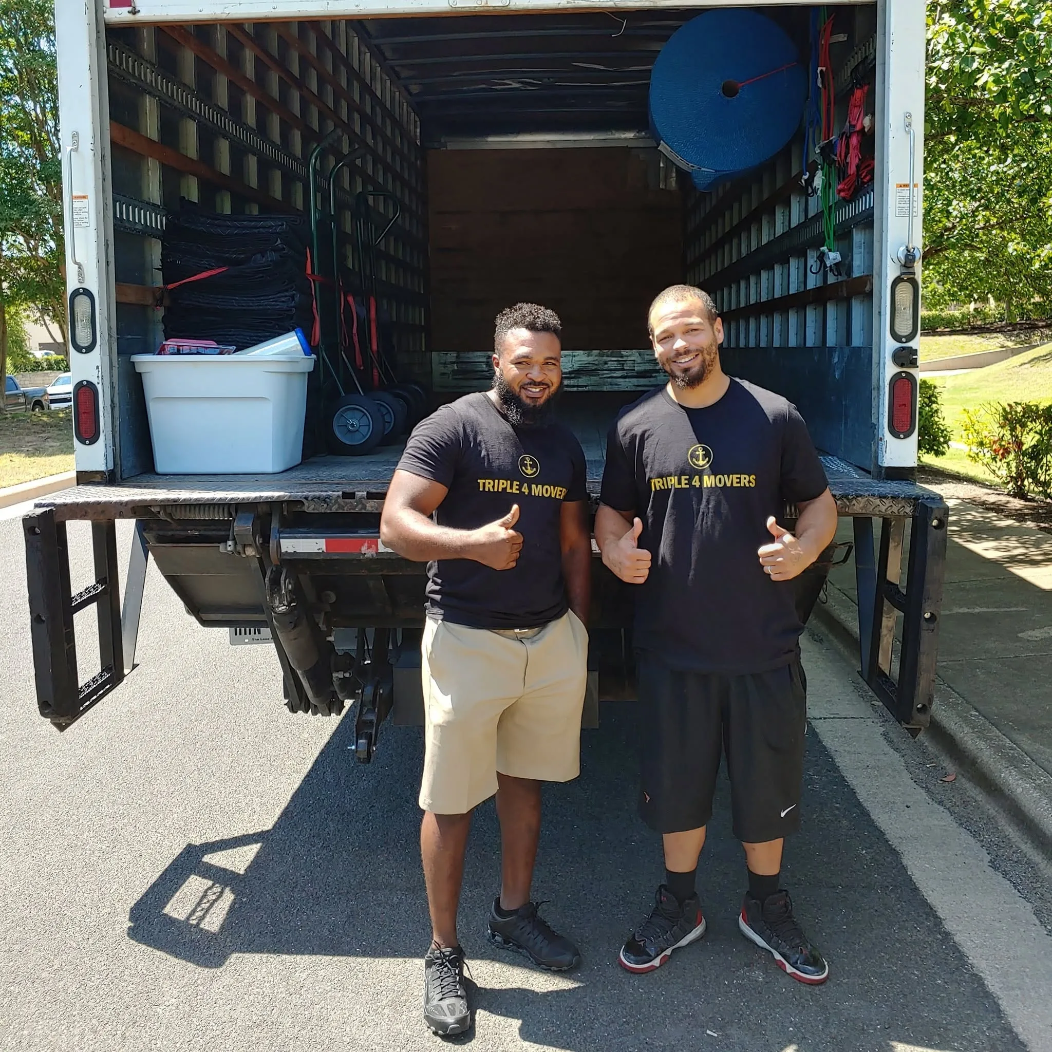 Two movers in Triple 4 Movers branded shirts give thumbs up in front of a loaded moving truck.